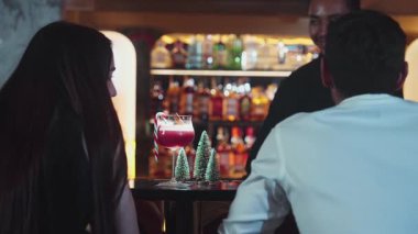 Barmen kokteyl temalı karışık kokteyl servis ediyor. Karışık kokteyl temalı. Karışık kokteyl çubuğuyla süslenmiş yeşil neon karlı Noel ağacında içki içen bir kadına servis ediliyor. Vinosity.