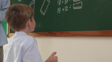 Düşük açılı kamera, yetenekli öğretmen çocuğa bakarken beyaz çocuğun tahtaya cevap yazdığını gösteriyor. Sorulara cevap vermek için gönüllü olan zeki ilkokul öğrencilerini kapatın. Eğitim. Pedagoji.