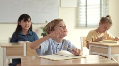 Kafkasyalı zeki çocuk, ilkokulda öğretmenlerin geçişi sırasında sınıfta okuyan çeşitli çocuklarla çevrili öğretmenlere sorduğu ve cevap verdiği için elini kaldırıyor. Eğitim konsepti. Pedagoji.