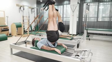 Müşteri, spor salonundaki yenilikçi bir makinede kayışla ters bacak kaldırma hareketi yapıyor. Çekirdek bağlantısını, dengesini ve esnekliğini geliştirmek için ters takla atan iki mutlu antrenör. Alışkanlık.