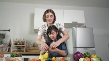 Zeki beyaz anne ve Asyalı kız birlikte yemek pişiriyor ve sebze doğruyor ya da akşam yemeği için salata hazırlıyor. Mutlu anne ve kız taze yemekle sağlıklı yemek yapıyorlar. Eğitim konsepti. Pedagoji.