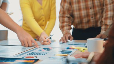 Bir grup profesyonel, modern bir ofiste stratejik karar verme mekanizmasını geliştirmek amacıyla tabloda sergilenen veri raporlarını işbirliği içinde analiz ederek grafikler ve grafikler üzerinde çalışıyor. SACTR