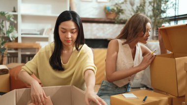 Çekici bir oda arkadaşı oturma odasında paket paketlerken pakette konum yazıyor. Mutlu satıcı birlikte çalışıyor ve teslimat paketini hazırlıyor. Girişimci kargo kutusu paketliyor. Myrmidon.