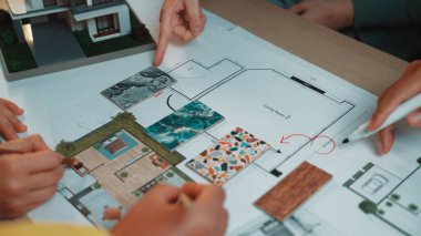 Bir ev yenileme projesinde işbirliği yapan bir grup profesyonel, ayrıntılı kat planlarını analiz ediyor ve tasarım unsurları, renk örnekleri ve materyalleri tartışıyor. SACTR
