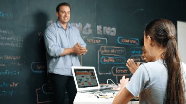 Kafkas öğretmeni alkışlayarak öğrencileri kodlamayı veya programlamayı teşvik etmek için alkışlıyor. Çeşitli öğrenciler STEM sınıfına katılırken başarılı bir projeyi kutlamak için el çırpıyorlar. Öğretim.