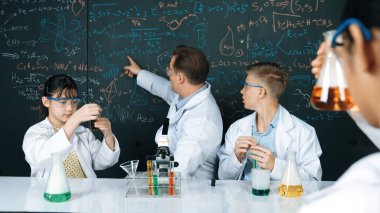 Zeki öğretmen, öğrenci renkli çözeltileri karıştırırken ya da deney yaparken kimyasal teoriyi açıklar. BTMM fen dersinde karatahtaya işaret ederken, eğitmen kimya öğretiyor. Öğretim.