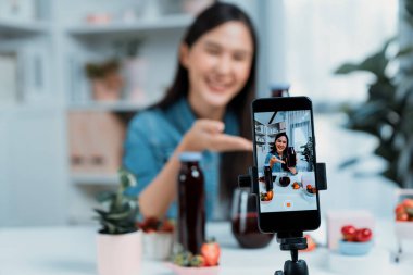 Seçici odaklı akıllı telefon ve gülümseyen genç, güzel Asyalı karışık çilek ve kiraz suyu detoksu değerlendirmesi sosyal medyada sağlıklı ürün tanıtımı sunuyor. Taktik.