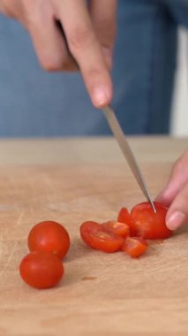 Close up hands holding a knife preparing a contented meal. Sliced tomatoes and other vegetables on the glass dish.
