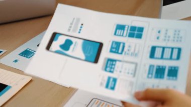 Mobil uygulama için kullanıcı arayüzü prototipini ofis çalışanlarına sunan harika bir şirket çalışanı. UX UI tasarımcısı kağıt üzerinde simge tasarımının işlevini açıklıyor. Sinerjik