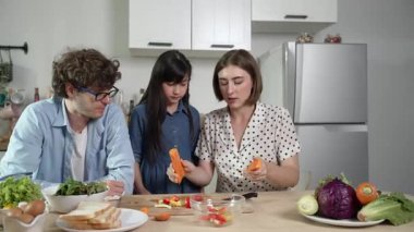 Çekici beyaz anne ve baba Asyalı kızıyla taze yemek pişirmek için birlikte vakit geçiriyorlar. Enerjik anne ve baba mutfakta salata yapmak için taze sebze hazırlıyor. Sağlıklı yiyecekler. Pedagoji.