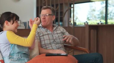 Grandfather and granddaughter eat french fries watch interesting entertainment on TV. Senior use technology communicate with young generation cross generation gap strengthen family bond. Divergence.