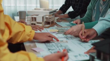 Yenilikçi bir çalışma alanında yaratıcılığı ve takım çalışmasını vurgulayan, tasarım çizimleri ve modelleri üzerinde işbirliği yapan dinamik bir mimari ekibini gösteren canlı bir sahne. SACTR