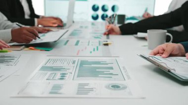 Çeşitli profesyonellerden oluşan bir grup, haritalar ve grafiklerle çevrili modern bir ofis ortamında işbirliği yaparak, veri odaklı içgörülere odaklı stratejik bir iş toplantısı düzenliyor. SACTR