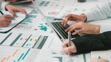 Raporlar ve çizelgeler ile işbirliği içinde çalışan ellerin yakın plan görüşü, modern bir ofis alanında takım çalışması ve stratejik planlamayı vurguluyor. SACTR