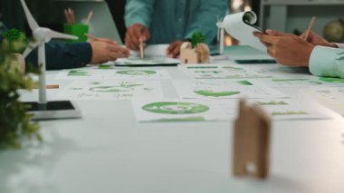 Bir grup profesyonel, sürdürülebilir projeler üzerinde yoğunlaşarak çağdaş bir ofiste işbirliği yapıyor. Belgeler, çizelgeler ve planlar yayılmış, yenilik ve takım çalışması sergileniyor. SACTR