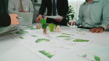 Profesyonel bir iş ekibi, yeşillik ve işbirlikçi enerjiyle çevrili modern bir ofiste grafikler ve grafikler etrafında verimli bir tartışmaya girişir. SACTR