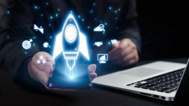 Bir işadamı akıllı telefondan fırlatılan dijital bir roketi, yenilikleri ve modern iş ortamlarında teknolojinin dönüştürücü gücünü sembolize ediyor. Dörtgen