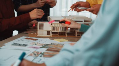 Bir grup profesyonel, işbirliği ve beyin fırtınası çabalarını geliştirmek için bir ölçek modeli, yapışkan notlar ve yaratıcı araçlar kullanarak mimari tasarım oturumuna katılıyor. SACTR