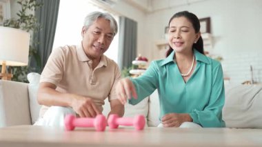 Mutlu yaşlı çift evde dambıllarıyla egzersiz yapıyor, kas gücü, eklem sağlığı ve sağlıklı yaşlanma için fiziksel sağlığa odaklanıyor. Emeklilik konsepti. Myrmidon.