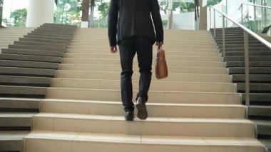 İş adamının bacağına yakın çekim merdivenleri çık. Başarılı bir adam merdivenleri çıkarken yeni bir şey keşfediyor. Seyahat etmek, terfi almak, yeni bir iş bulmak, yeteneğini artırmak. Arkadan bak. Sevinçli..