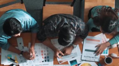 Tasarımcı fikirleri yazarken proje yöneticisinin yukarıdan aşağıya bakan görüntüsü. Akıllı iş adamları logo tasarımı fikrini açıklarken tasarımcılar palete bakarken temayı seçiyorlar. Sempozyum.