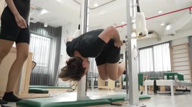Profesyonel pilates eğitmeni, bir müşteriye jimnastik salonunda pilates yaparken rehberlik ediyor. Çekirdek dengesini ve omurilik hizasını iyileştirmek için çubuğa tutunan bir adam. Sağlıklı olmak. Alışkanlık.
