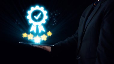 Takım elbiseli bir iş adamı, modern teknoloji ortamında başarı, kalite ve yeniliği temsil eden yıldızlı bir dijital ödül sembolü sergiliyor. Dörtgen