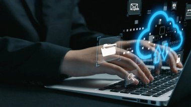 Bir dizüstü bilgisayarın klavyesine yazı yazan, veri yönetimi ve çevrimiçi iletişim gerekliliklerini temsil eden bulut teknolojisi simgeleri ve dijital sembolleri gösteren bir yakın çekim. Dörtgen