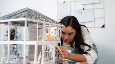 Genç, beyaz, güzel mimar mühendisi ev modelini ev inşaatını teftiş etmek ve sorunu modern ofisteki toplantı masasında çözmek için hata noktasını kontrol etmek üzere çeviriyor. - Yakın çekim. Tertemiz..