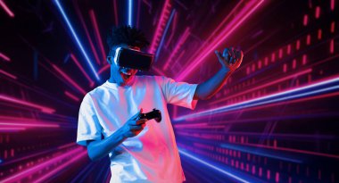 Neon soyut arka planda oyun oynarken elinde joystick tutan ve VR gözlük takan bir genç. Afrikalı adam kontrol etmeyi ve artırılmış gerçeklik teknolojisini kullanmayı seviyor. Yaratıcılık.
