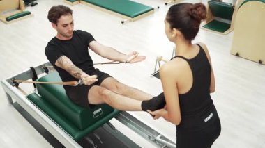 Beden eğitiminde birlikte pilates egzersizi yapan birkaç mutlu antrenör. Çekirdek gücü ve dengeyi arttırmak için reformcuda yüz poz veren İspanyol bir adam. Alışkanlık.
