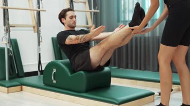 Erkek müşteri pilates ark fıçısında bacak kaldırma alıştırması yapıyor. Vücut dengesini, bacak dayanıklılığını ve spor salonundaki esnekliğini arttırmak için eğitmen yardımı ile birlikte. Öğrenci yalancı ve muziplik pozu veriyor. Alışkanlık.