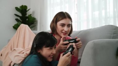 Annem dizüstü bilgisayar kullanarak kanepeye uzanırken, mutlu kız oyun oynuyor ve oturuyor. Beyaz bir ebeveyn ve çekici bir kız, elinde joystick ile birlikte vakit geçirir ve maç kazanmaya odaklanırlar. Pedagoji.