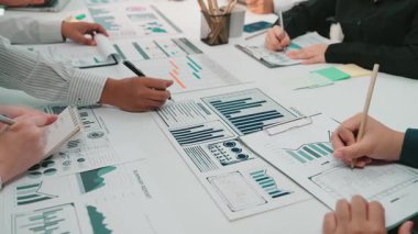 Bir iş toplantısında yer alan bir grup profesyonel, belgelerde gösterilen çeşitli tablo ve grafikleri analiz ederek, çağdaş bir ofis ortamında işbirlikçi karar verme mekanizmasını vurguluyor. SACTR