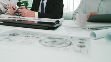 Bir grup iş adamı modern bir ofis ortamında ortak bir toplantıya katılıyor. Belgeleri gözden geçirir, dijital cihazlar kullanır ve proje stratejilerini tartışırlar. SACTR