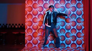 Asyalı break dansçı serbest stile geçiyor ve balon arka planlı kameraya bakıyor. Profesyonel hippi gündelik kıyafet giyer ve gözlük takar. Mutluluk.