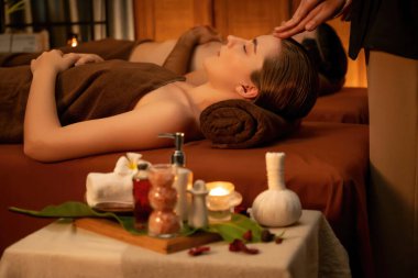 Stres önleyici kafa masajının keyfini çıkaran ve lüks otel veya otellerde sıcak mum ışığında cilt bakımını şımartan bir çift müşteri. Sessiz.