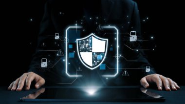 Siyah takım elbiseli profesyonel bir adam dijital elementlerle çevrili siber güvenlikle meşgul. Kalkan grafiği veri korumasını ve çevrimiçi güvenlik önlemlerini sembolize eder. Dörtgen