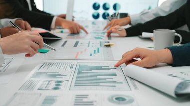 Bir masadaki veri tablosu ve grafiklerinin analizi ile uğraşan çeşitli ellerin yer aldığı ortak bir iş toplantısı. Profesyoneller strateji ve içgörü konusunda işbirliği yaparlar. SACTR