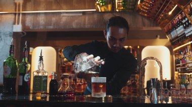 Asyalı barmen soğuk bardağa karışık viski dökerek soğutmalı buzlu içecek üretiyor. Lüks ılık barlarda alkol yenileme gösterisine odaklanan yaratıcı bir reklam yapıyor. Vinosity.