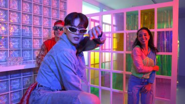 Asyalı adam gece kulübünde çeşitli neon ışıklarda dans ederken kolunu oynatıyor. Modern kulüpte çok kültürlü hippilerle dans eden şık elbiseli mutlu dansçı. Mutluluk.