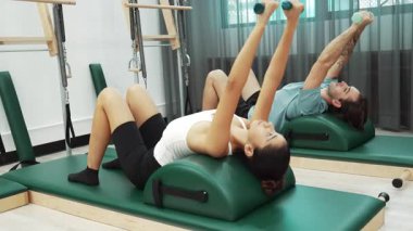 Müşteriler pilates ark fıçısı ekipmanları üzerinde küçük ağırlıklar kullanarak kol ve bacak esnemeleri yapıyorlar. Antrenörlerden bir kaçı sırt, kol ve bacak ağırlıkları ile çekirdeği ve dengeyi geliştiriyor. Alışkanlık.