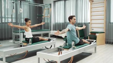 Pilates reformatör makinelerinde senkronize kol uzantıları yapan iki müşteri. Mutlu pilates partnerleri, esnekliği arttırmak ve dengeyi ve kontrolü sağlamak için reformcunun üzerine oturdular. Alışkanlık.