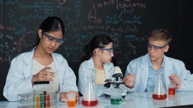 Akıllı genç kız kimya teorisi ile tahtayı dikkatlice incelerken mikroskop altında numune bırakıyor. Profesyonel bilim adamı tüpün içine kimyasal madde döker ve deney için hazırlanır. Öğretim