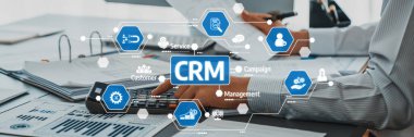 Bir iş adamı, CRM simgeleri ve diyagramları arasında bir hesap makinesi ile etkili yönetim stratejileri ve çağdaş ofis ortamında müşteri ilişkileri göstererek etkileşime girer. Dostluk