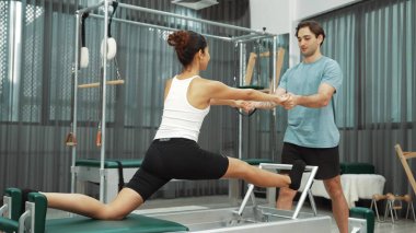 Esneklik ve çekirdek eğitimi için pilates kursunda trapez masasında destek alan bir kadın. Öğrenci dengeyi geliştirmek için reformcuları iki büklüm ediyor. Alışkanlık.