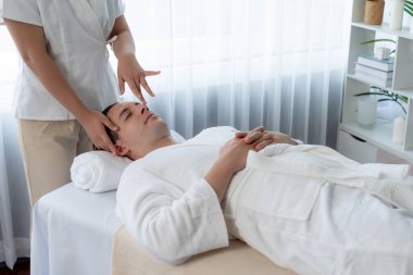 Beyaz adam stres önleyici kafa masajından ve lüks bir tatil beldesi veya otel spa salonundaki modern ışık ortamında yüz güzelliği eğlencelerini şımartmaktan hoşlanıyor. Sessiz.