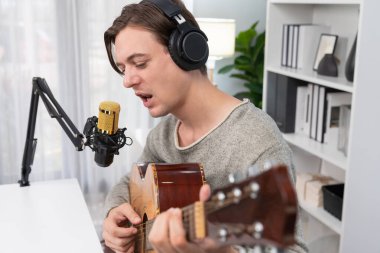 Gülümseyen yüzlü akıllı şarkıcının sunucu kanalı, şarkı söylerken gitar çalmak, sosyal medya kanalında yayın yapmak, modern stüdyo kaydında video kaydedici olarak kulaklık takmak. Bireysel.