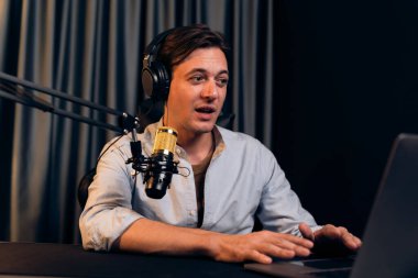 Sunucu kanalı akıllı yayıncı laptopta canlı sosyal medya uygulaması arıyor, kulaklık takıyor ve modern ofis stüdyosundaki mikrofonu kullanıyor. Bireysel.