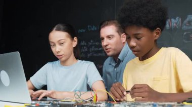 Kafkas öğretmeni mühendislik kodlarını öğretirken dizüstü bilgisayarı gösteriyor. Lise öğrencisi mutlu bir şekilde öğrenirken ve programlama öğrenirken bilgisayar kullanarak çalışan eğitmen. Öğretim